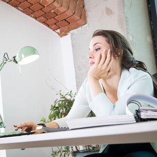 Eine Frau schaut in einem Büro gelangweilt auf ihr Notebook | Verhaltenstherapeut über Erwartungsdruck und Selbsthärte: So gelingt ein Jahresrückblick ohne Druck