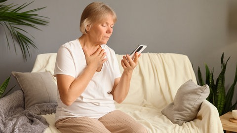 Frau sitzt auf der Couch mit Telefon in der Hand