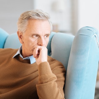 Mann sitzt traurig im Sessel