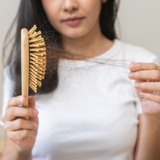Eine Frau schaut besorgt auf eine Bürste voller ausgefallener Haare.