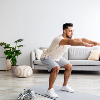 Mann macht im Wohnzimmer Kniebeuge