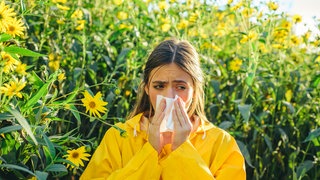 Frau steht in Blumenfeld und putzt sich die Nase