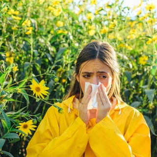 Frau steht in Blumenfeld und putzt sich die Nase