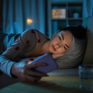 Frau sieht aufs Handy und liegt im Bett 