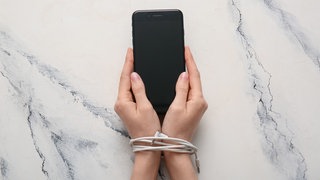 Handy in der Hand und Ladekabel um die Handgelenk