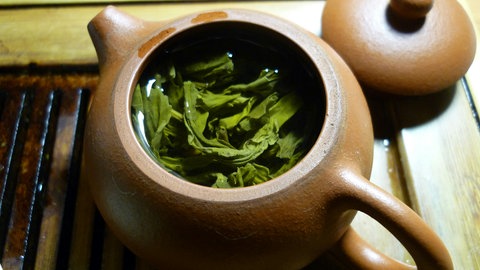 Große Teeblätter von Grüntee schwimmen in brauner japanischer Teekanne. Wie gesund sind grüner Tee und Matcha tatsächlich?