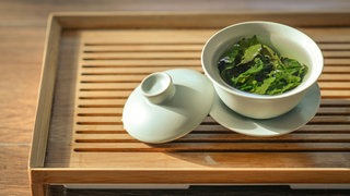 Große Blätter grünen Tees schwimmen in japanischer weißer Porcellanschale. Wie gesund sind grüner Tee und Matcha tatsächlich?