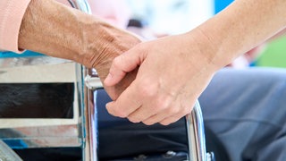 Nahaufnahme eines Pflegepersonals, das die Hand eines älteren Patienten in einem Rollstuhl hält, der Unterstützung und Hilfe während der Rehabilitation bietet. | Pflege auf dem Land: Wie Gemeindeschwestern Senioren helfen