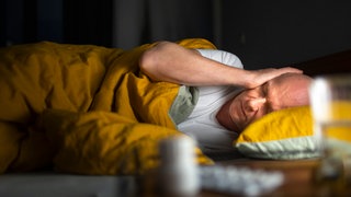 Mann liegt im Bett und hält sich die Ohren zu. Eine neue Studie der Universitätsmedizin Mainz zeigt, dass bereits moderater Straßenlärm bei Nacht den Körper stresst.