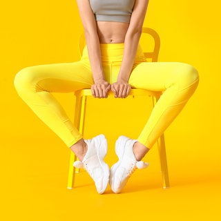 eine Frau sitzt vor gelbem Hintergrund in Trainingskleidung auf einem Stuhl