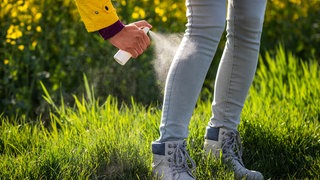 Frau sprüht ihre Hose mit Insektenschutz ein