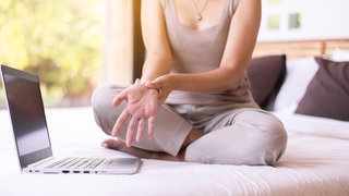 Frau sitzt auf Bett und bewegt ihr Handgelenk