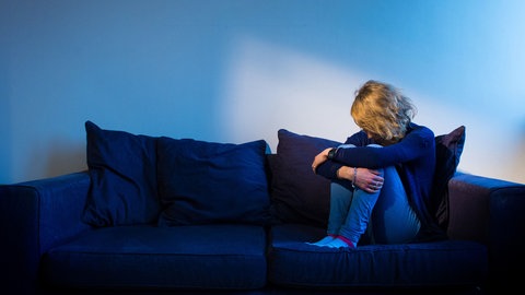 Eine Frau sitzt in bedrückter Haltung auf einer Couch. Könnte das in sogenannten Magic Mushrooms enthaltene Psilocybin bei therapieresistenten Depressionen helfen?
