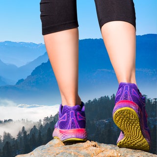 Frau steht auf einem Felsen. Im Hintergrund sieht man die Berge