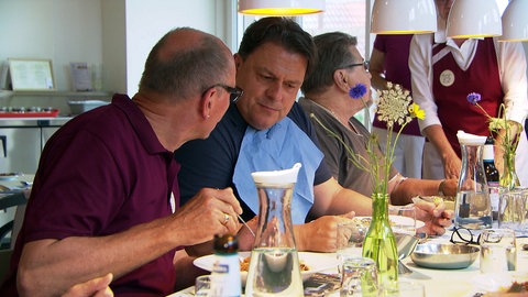 Menschen sitzen in Harpolingen an einem Tisch, essen zu Mittag und unterhalten sich.