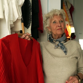 Sabine Lynch steht vor ihrem Kleiderschrank und zeigt ein rotes Kleid.