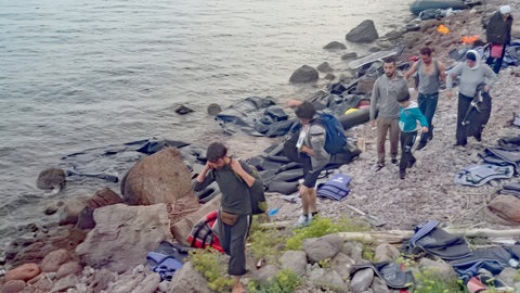Geflüchtete Syrer auf der griechischen Insel Chios. Auf einem felsigen Strand liegen Rettungswesten und Reste eines Schlauchboots. SWR1 Neuanfang. Mohamed: Flucht in ein neues Leben – ein junger Syrer schwimmt sich frei. Mohamed hat den syrischen Bürgerkrieg überlebt und fand eine neue Heimat in Stetten im Remstal. Warum ein Schwimmbad dabei entscheidend geholfen hat, erzählt er in SWR1 Neuanfang.