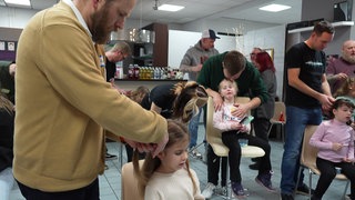 In einem Friseursalon in Bad Kreuznach wird Männern erklärt, wie man mit langen Haaren umgeht und sie frisiert.