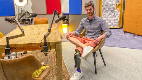 Felix im Jahr 2026: Er sitzt zum Interview im SWR1 Studio und lächelt in die Kamera. Sein rechtes Bein hat er über die Prothese geschlagen.