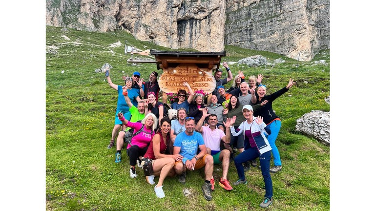 Eine Gruppe Wanderer hat sich um eine Höhenmarkierung auf den Dolomiten gruppiert und jubelt. Stefan Kappler hat ALS und kann deshalb nicht mehr in den Bergen wandern. Seine Freunde machen mit ihm die ersehnte Tour durch die Dolomiten. Wie er es schafft, trotz der Amyotrophe Lateralsklerose (ALS) seine Lebensfreude zu behalten, erzählt er in der Audioreihe  Podcast SWR1 Neuanfang.