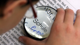 Ein sehbehinderter Schüler liest während des Sprachunterrichts mit Hilfe einer Lupe einen Text. 