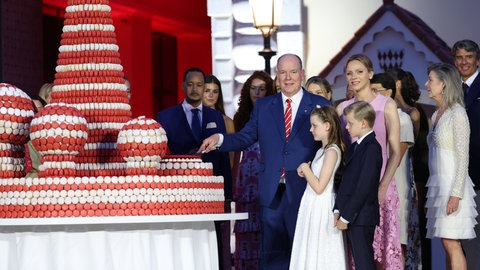 Fürst Albert II. schneidet zu seinem 20-jährigen Thronjubiläum eine riesige Torte an. Neben ihm stehen seine Frau Charlène und die beiden Kinder.