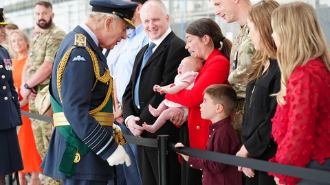 König Charles III. trifft während eines Besuchs bei der Royal Air Force Soldaten und ihre Familien. Er schaut in Uniform auf eine Mutter mit ihrem schreienden Kind. 