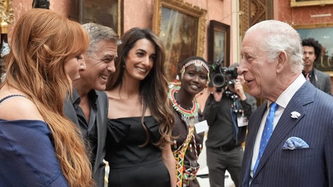 König Charles reicht einer Dame die Hand, daneben stehen George Clooney und seine Frau Amal.