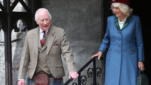 König Charles und Königin Camilla beim Gottesdienst zu ihrem 20. Hochzeitstag. Charles trägt ein braun-kariertes Sakko mit Weste und Schottenrock. Camilla trägt ein blaues Kleid mit rotem Hut.