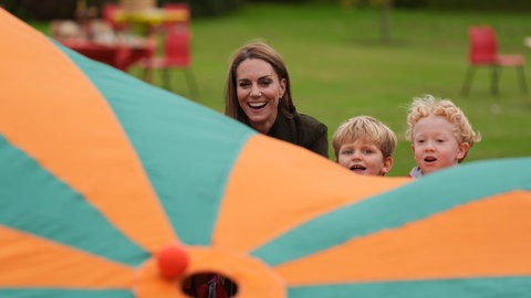 Prinzessin Kate lässt mit Kindern zusammen kleine Bälle auf einem großen bunten Tuch hüpfen, dass sie festhalten.