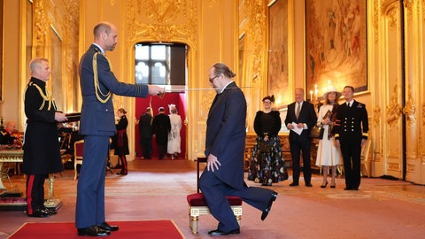 Prinz Willliam schlägt den knienden Schauspieler Gary Oldman in einem prachtvollen Saal auf Schloss Windsor mit einem Säbel zum Ritter . 