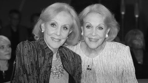 Alice und Ellen Kessler stehen nebeneinander und schauen zusammen in eine Richtung an der Kamera vorbei, im Hintergrund ist Publikum zu sehen