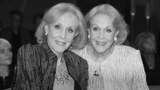 Alice und Ellen Kessler stehen nebeneinander und schauen zusammen in eine Richtung an der Kamera vorbei, im Hintergrund ist Publikum zu sehen