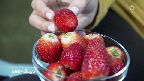 Hand greift in Glasschale mit Erdbeeren