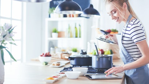 Eine Frau kocht und schaut sich ein Rezept auf dem Tablet an