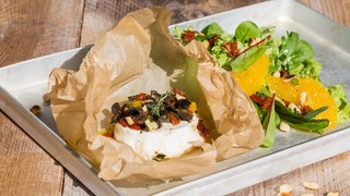 Ein runder Ziegenkäse, auf dem kleingeschnittenes Gemüse liegt, steht auf Pergamentpapier