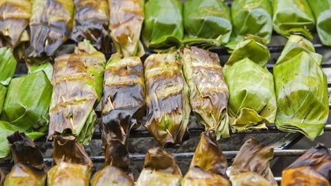 Rundes Grillgut in Bananeblättern verpackt auf dem Grillrost.