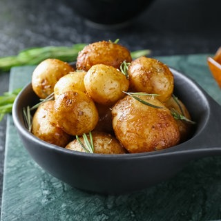 Bratpfanne mit gebackenen Kartoffeln und Rosmarin auf dunklem Hintergrund.