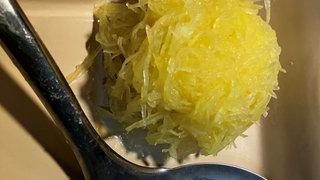 Zu sehen ist ein grüner Kloß aus rohen Kartoffeln, der auf einer Schöpfkelle liegt.