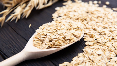 Ein Holzlöffel voll mit Haferflocken liegt auf einem Tisch