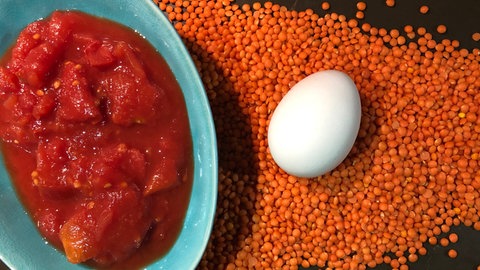 Dosentomaten in einer Schale, ein Ei und rote Linsen