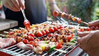 Männer am Grill marineiren Grillspieße