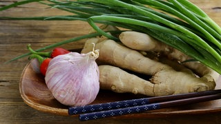 Knoblauch, Ingwer und Frühlingszwiebeln liegen zusammen mit Stäbchen in einer Holzschale
