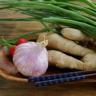 Knoblauch, Ingwer und Frühlingszwiebeln liegen zusammen mit Stäbchen in einer Holzschale