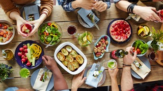 Ein gedeckter Tisch von oben, an dem verschiedene Menschen sitzen