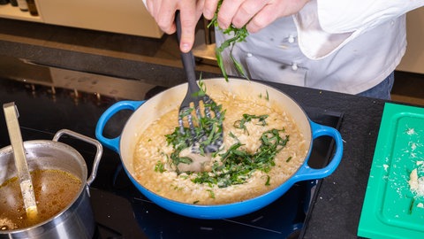 Das Risotto wird mit frischem Bärlauch in einem Topf abgeschmeckt.