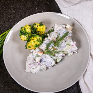 Der Heringssalat ist wie im Rezept beschrieben mit Pellkartoffeln auf einem Teller angerichtet.