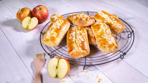 Apfeltasche aus Hefeteig garniert mit Mandeln liegen auf einem Rost: Mit diesem Rezept lässt sich das Gebäck ganz einfach selbermachen.