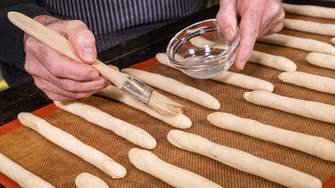 Die ungebackenen Hefeteigstangen, werden mit Wasser bestrichen.
