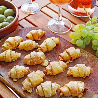 Holzbrett mit Käsehörnchen, daneben Trauben und ein Glas Rose-Wein